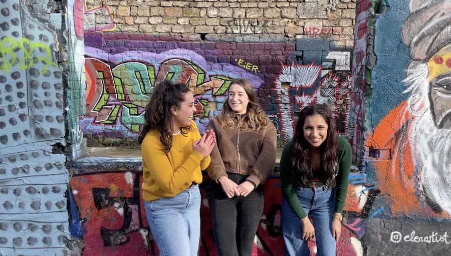 Trois étudiantes internationales souriant et riant devant des graffitis colorés à Bordeaux.