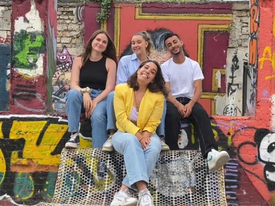 Quatre membres de l'équipe Dare&Go souriant et assis devant un graffiti coloré à Bordeaux.